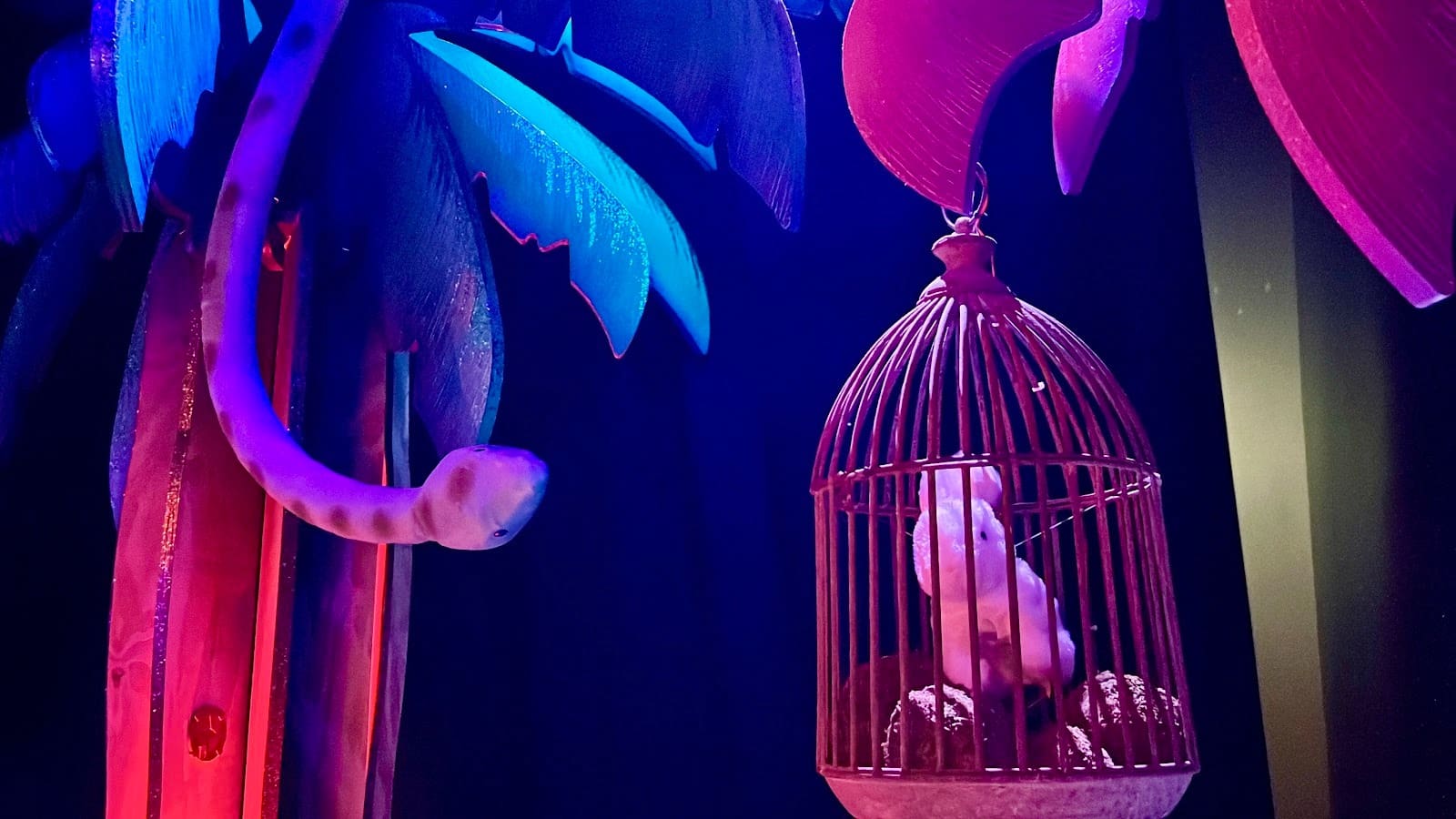Purple snake on a tropical tree watches a white mouse in a red cage. Neon colors create a mysterious, surreal mood.