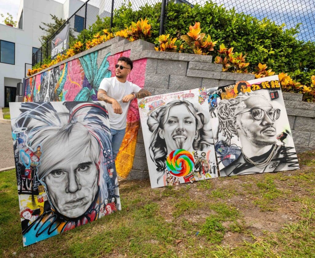 Michael Vahl stands with three large, colorful, street-art-inspired portrait paintings