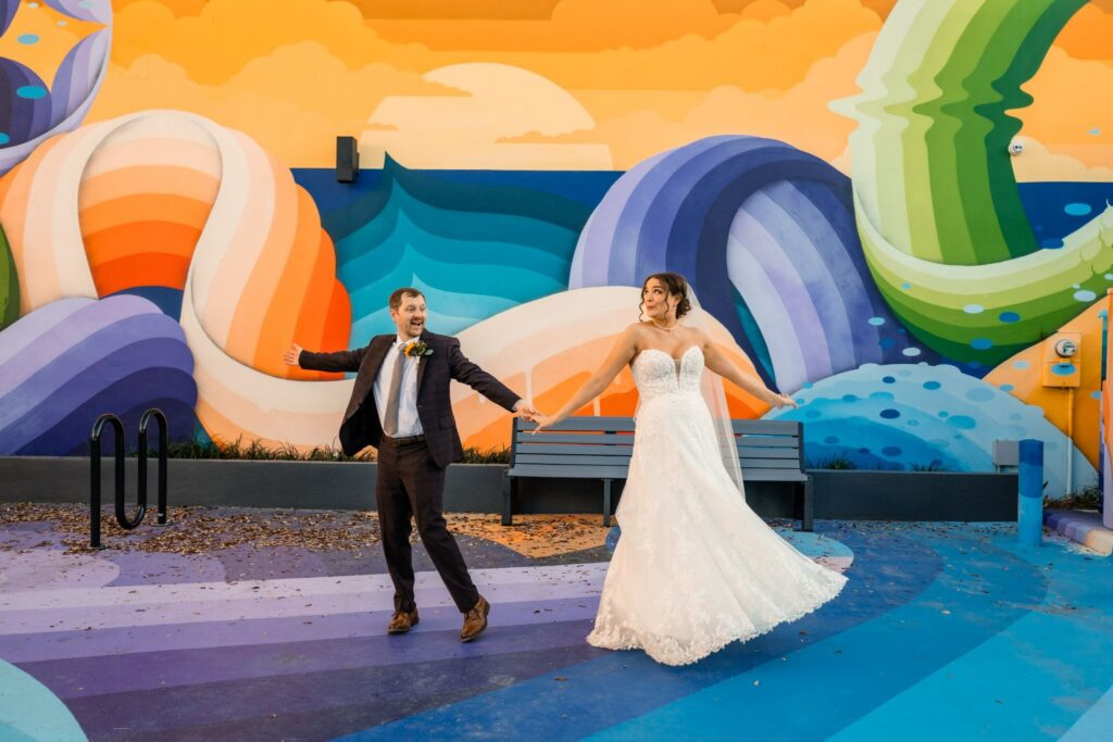 Bride and groom holding hands in front of a colorful mural at FloridaRAMA in St. Petersburg, FL