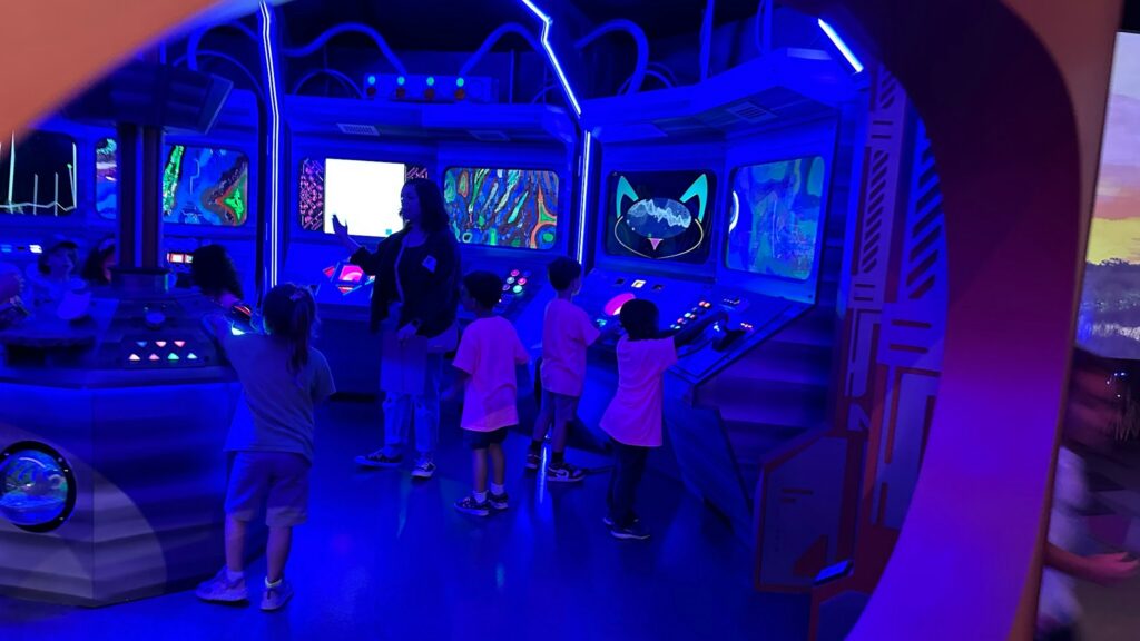 Children and a guide interact with a futuristic, neon-lit control panel exhibit at FloridaRAMA