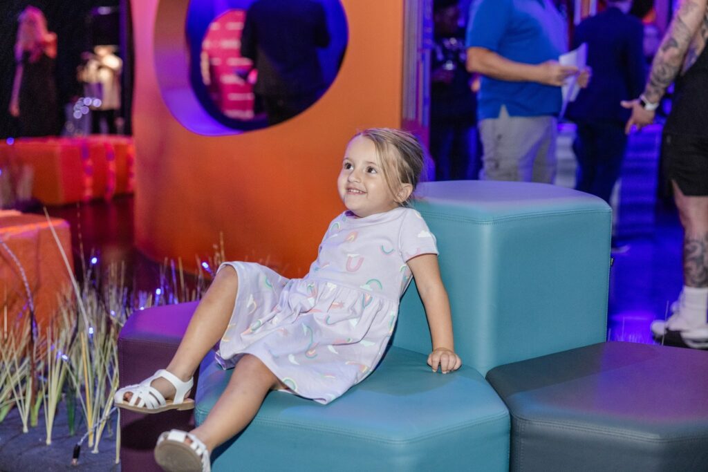 A young girl smiles with curiosity while exploring a colorful, immersive art installation