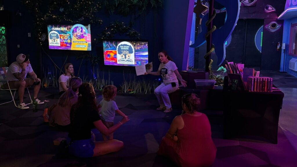 A guide reads a book to a family in an immersive storytelling exhibit with colorful lighting and screens