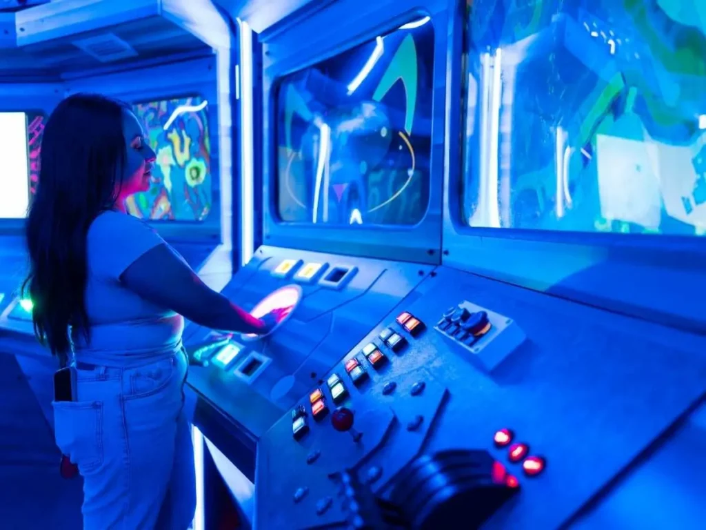 A visitor interacts with a neon-lit, futuristic control panel installation at FloridaRAMA