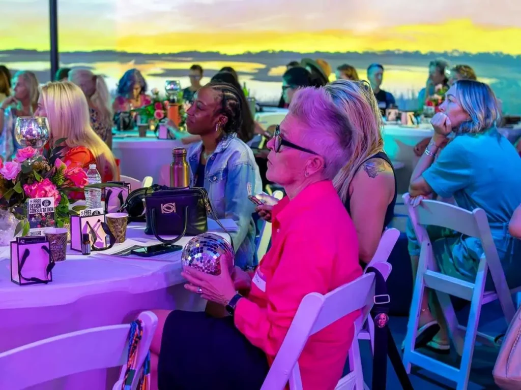 Guests at a social event in FloridaRAMA's immersive art space with a large sunset projection in the background
