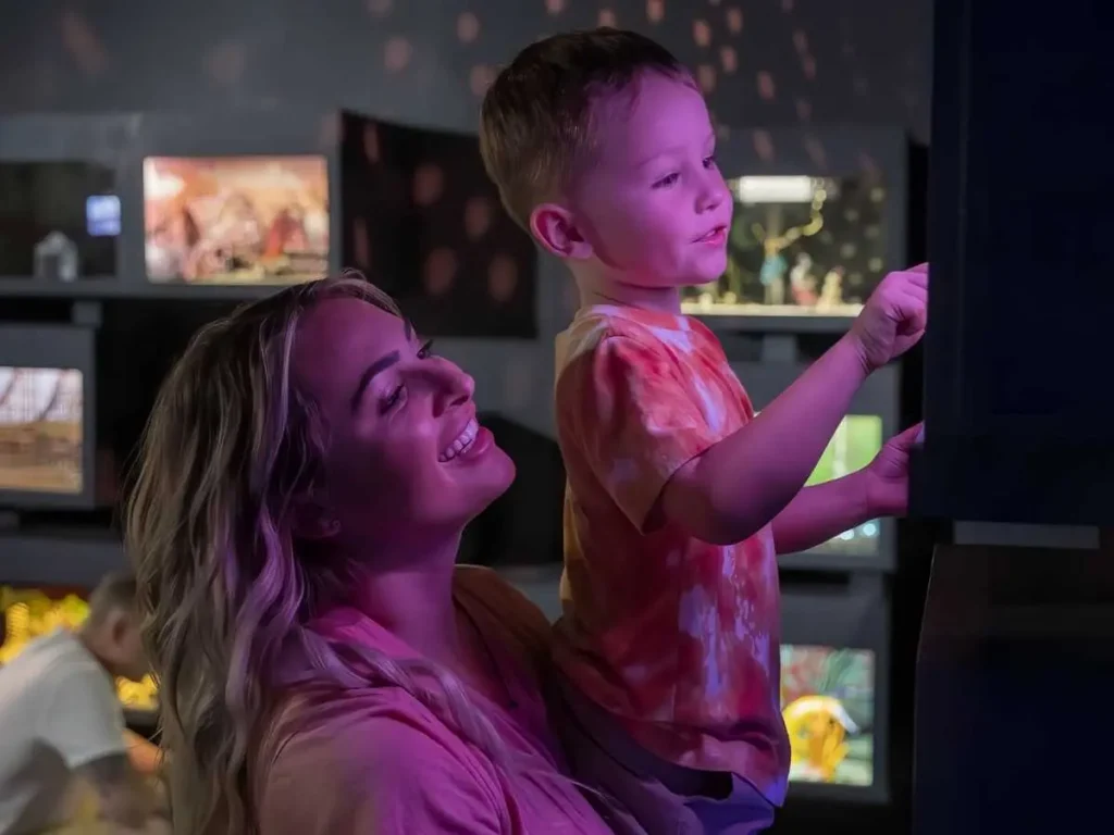 A woman holds a young child as they interact with a glowing art installation at FloridaRAMA