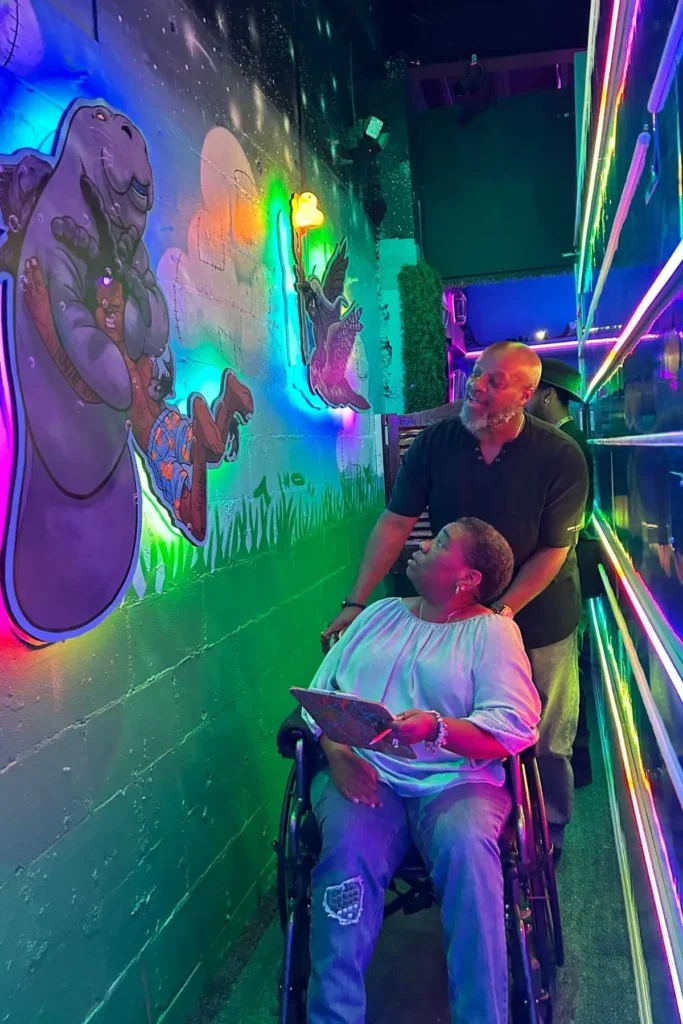A woman in a wheelchair and a man look at colorful artwork by iBoms aka Jabari Reed in an immersive art experience